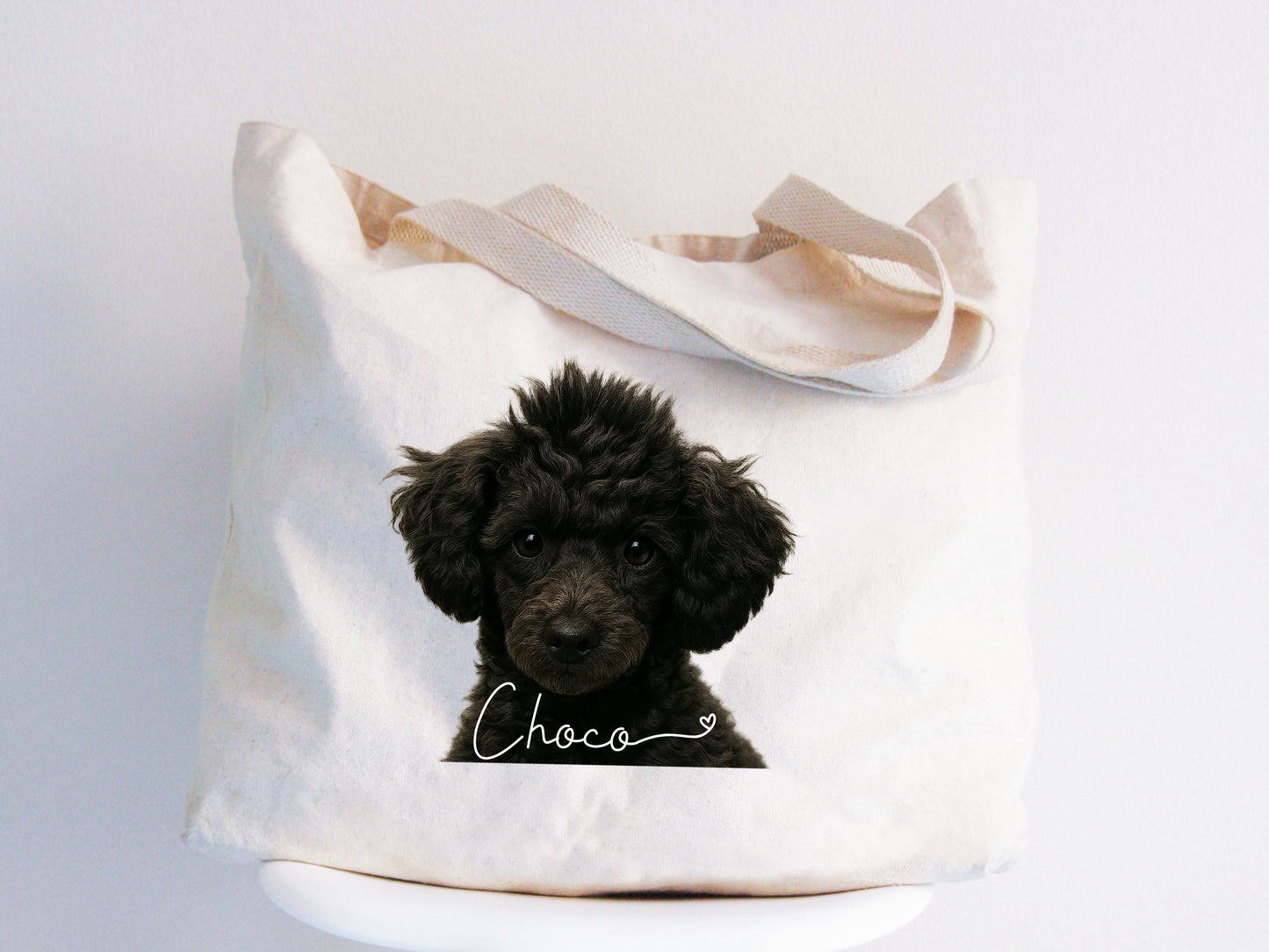 Large natural canvas tote bag featuring a hyper-realistic portrait of a black toy poodle named Choco, placed on a white chair. Custom pet jumbo tote bag by JupiterStarCo.